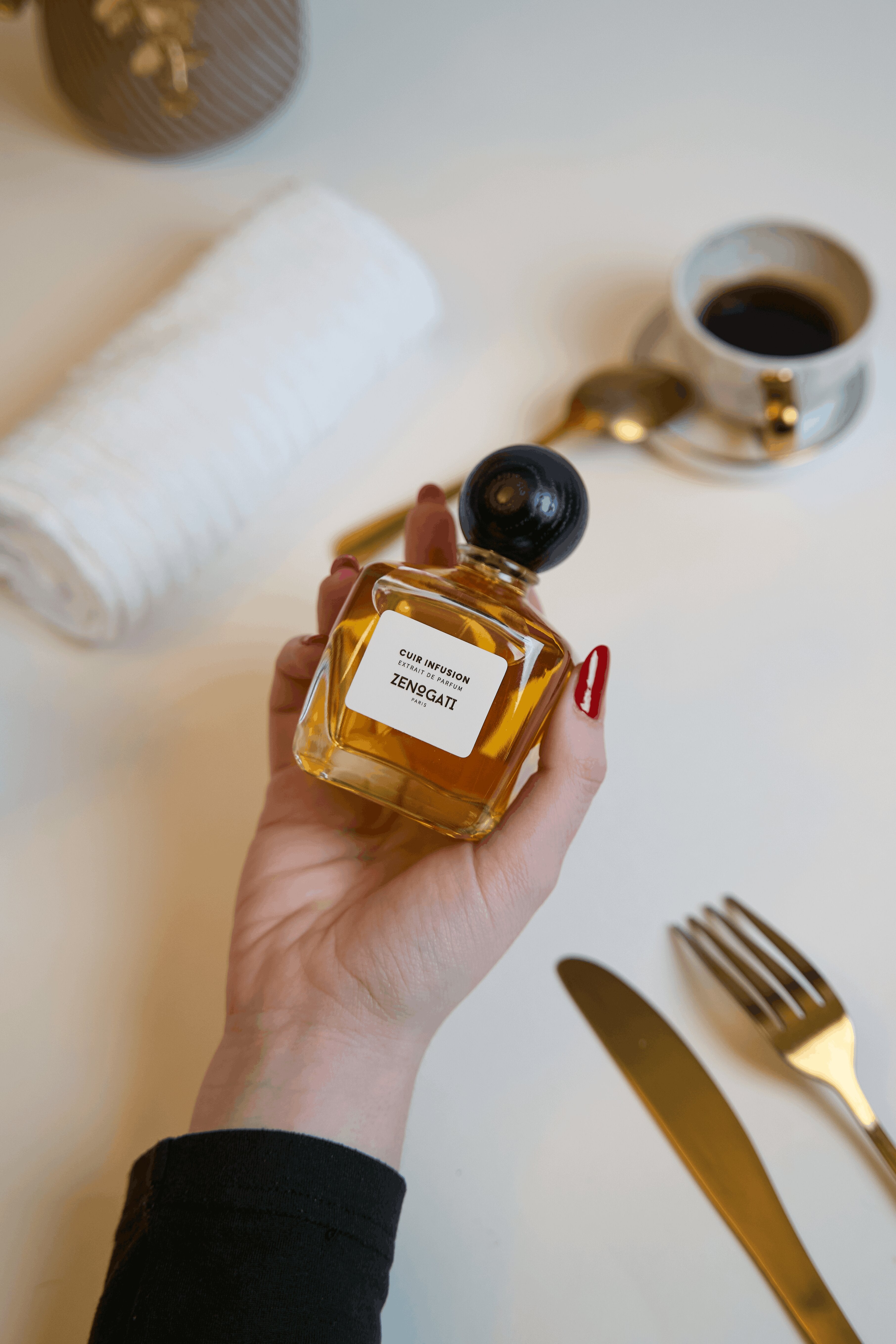 Flacon Zenogati Cuir Infusion tenu en main sur une table avec tasse de café et couverts