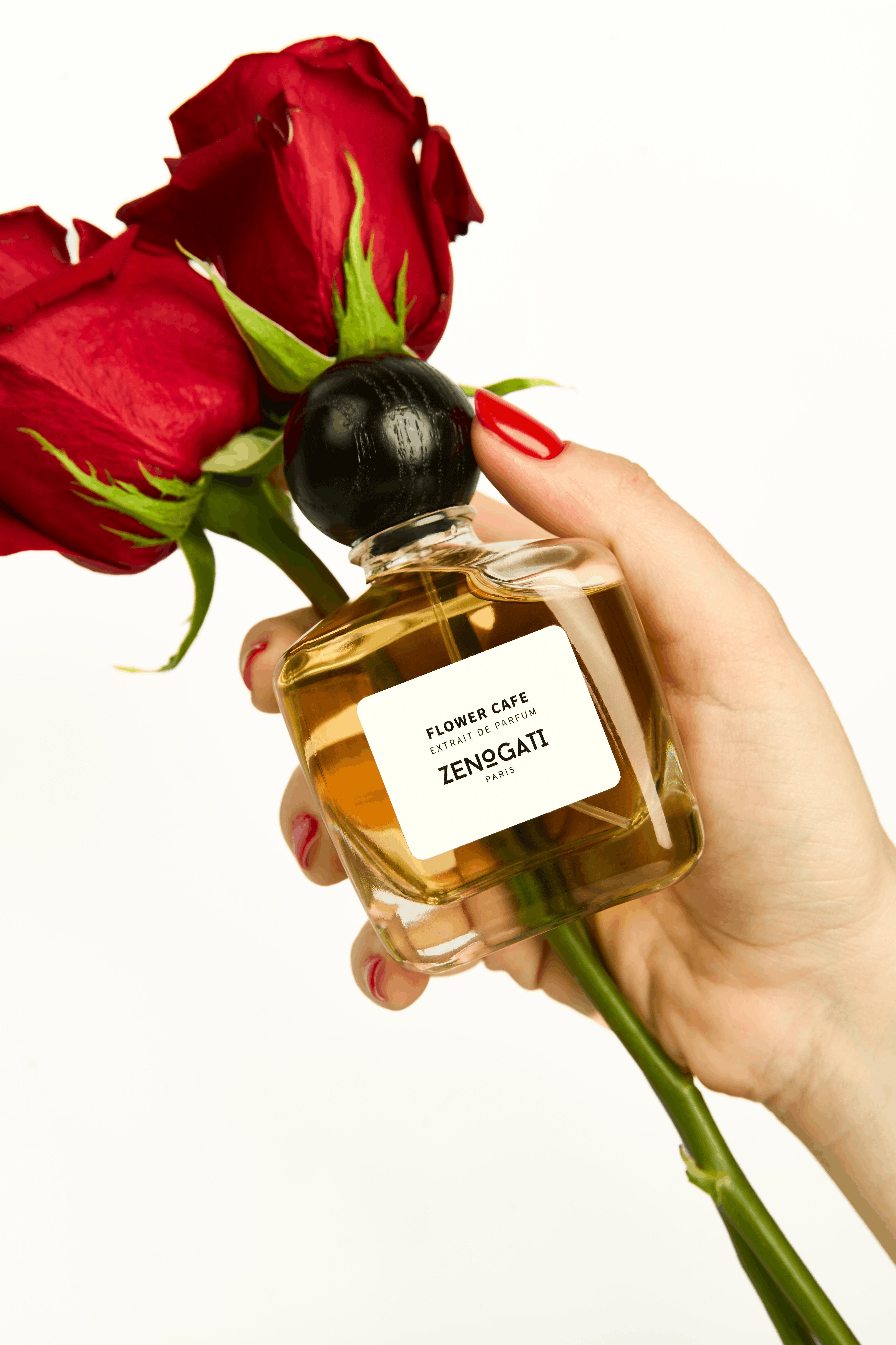 Flacon Zenogati Flower Café tenu en main avec des roses rouges, fond blanc